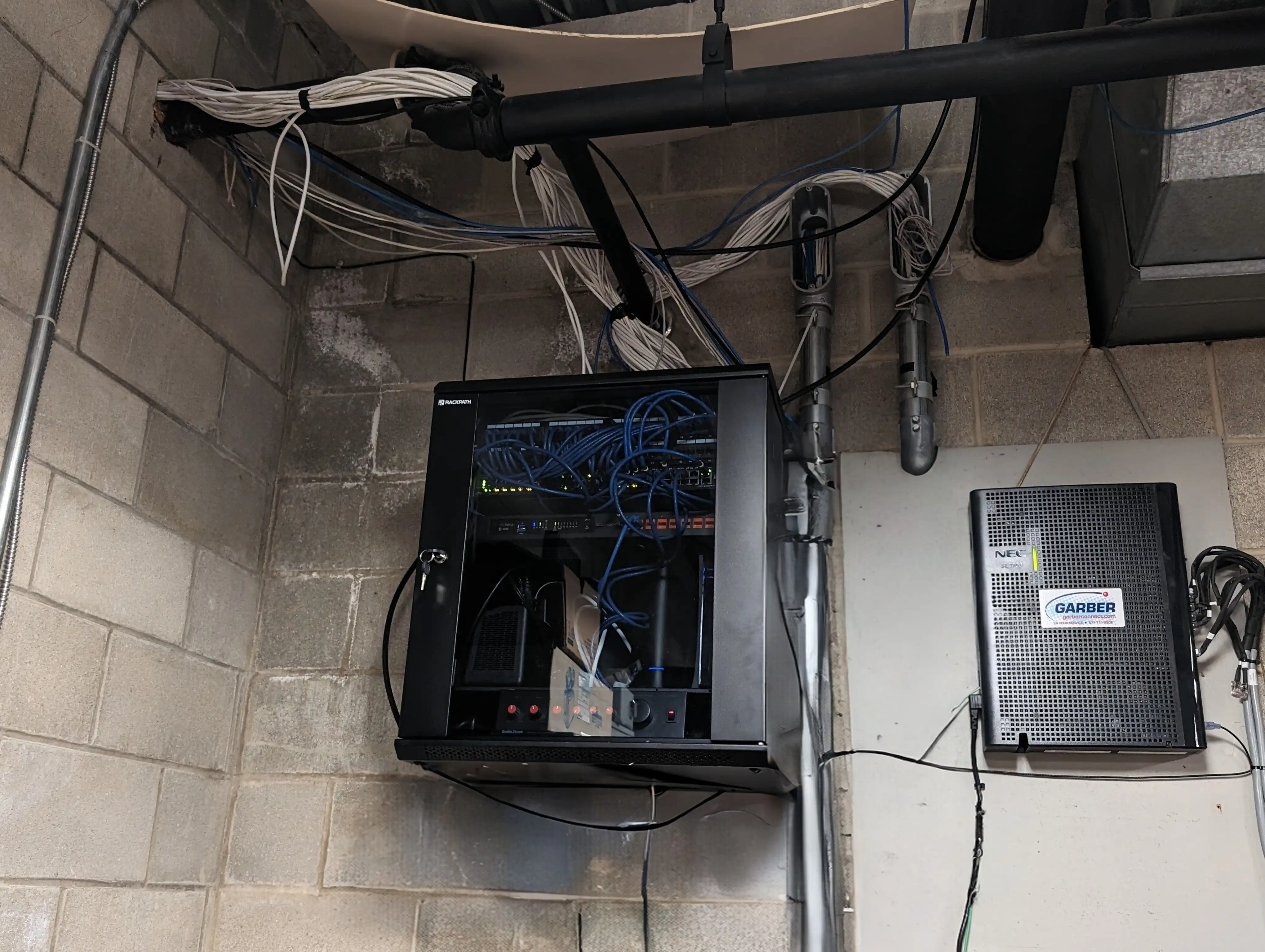 Professionally wall-mounted network equipment cabinet with organized blue Cat6 cables and NEC device at Springfield Family YMCA showing completed infrastructure installation