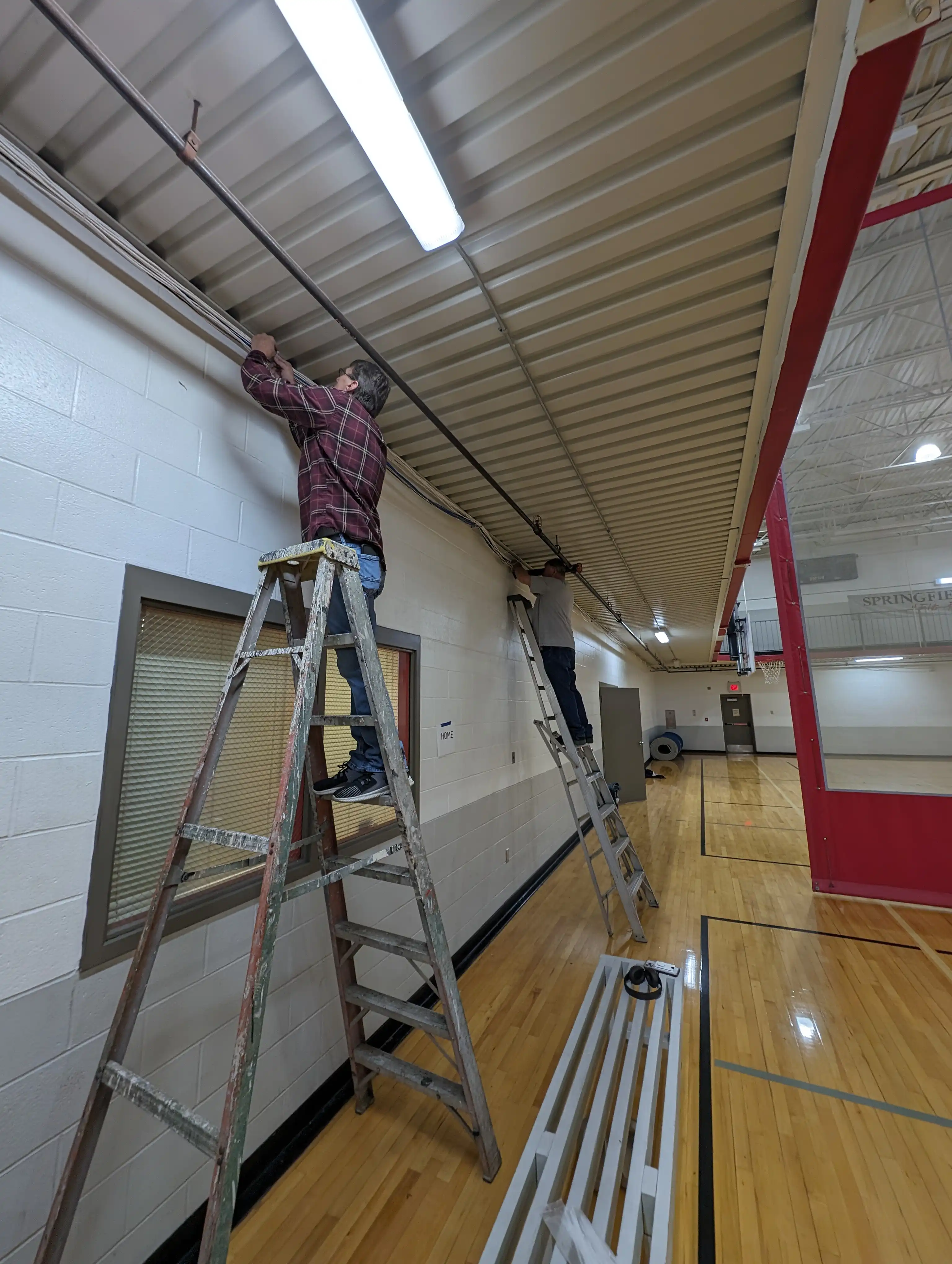 Network technician on ladder installing structured Cat6 cabling through ceiling plenum at Springfield Family YMCA gymnasium